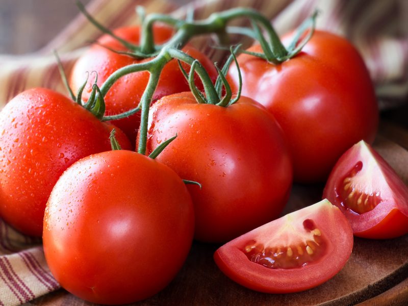 Fresh red ripe tomatoes on the vine on a dark rustic cutting board